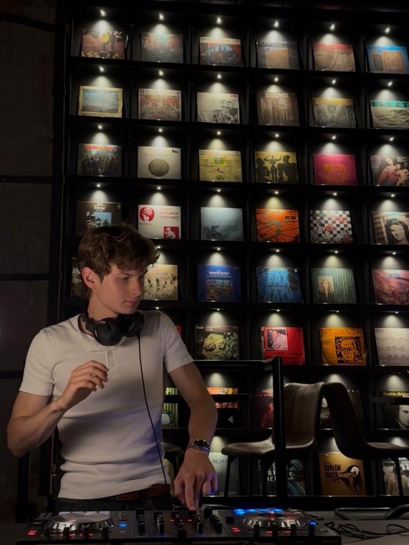 puntussoff behind the decks in front of a backlit wall of vinyl records, headphones around his neck, mid-set